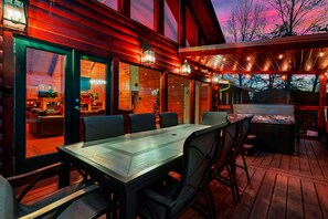 A wooden deck with a dining table and chairs, a hot tub, and a covered area with string lights. - NEW! Private 5BR, Sleeps 18, Six person Hot tub, Game Rm, Arcade (Sevierville)