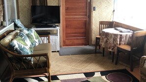 A compact living space with a television, a wooden door, a dining table with chairs, and a patterned rug. - A little piece of paradise in Ocean View with a view guesthouse! (OCEAN VIEW)