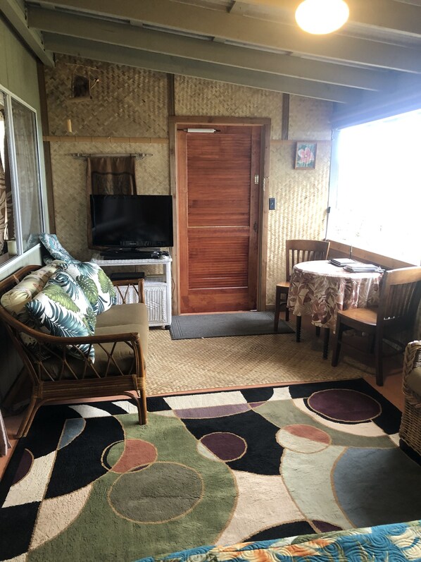 A compact living space with a television, a wooden door, a dining table with chairs, and a patterned rug.