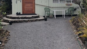 A single-story building with a gravel driveway, a wooden door, and a small patio area with a table and chairs. - A little piece of paradise in Ocean View with a view guesthouse! (OCEAN VIEW)