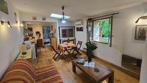 Un salon chaleureux avec un canapé, une table à manger et des chaises, une table basse en bois et une grande fenêtre donnant sur un paysage verdoyant.