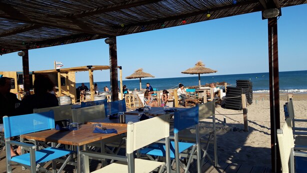 Un espace extérieur aménagé avec des tables et des chaises, une terrasse en bois et une vue sur la plage et l’océan.