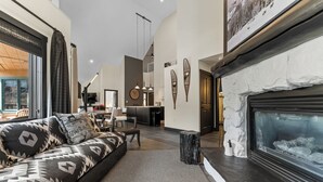 A modern living room with a fireplace, a sofa with patterned cushions, and a dining area in the background. - Arapahoe Lodge #8130 By Summit County Mountain Retreats (Keystone)