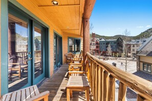 Um deck de madeira com cadeiras e mesas, com vista para uma cidade com edifícios e colinas.