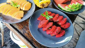 A wooden table with three plates of sliced fruits: yellow fruit, watermelon, and red fruit.