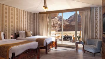 A hotel room with two beds, a large window with a desert view, a wooden floor, and a chandelier.