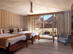 A hotel room with two beds, a large window with a desert view, a wooden floor, and a chandelier. - Shaden Resort (Al-'Ula)
