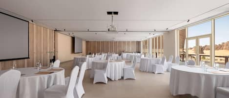 Una sala de conferencias con varias mesas redondas, sillas blancas y una pantalla grande.