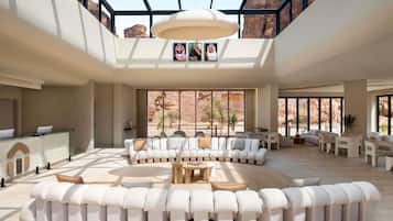 A spacious interior with a high ceiling, a central seating area, and large windows offering a view of rocky terrain.