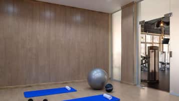 Uma academia com colchonetes de exercícios, halteres, uma bola de ginástica grande e uma TV fixada na parede.