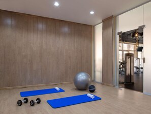 A gym with exercise mats, dumbbells, a large exercise ball, and a wall-mounted TV. - Shaden Resort (Al-'Ula)