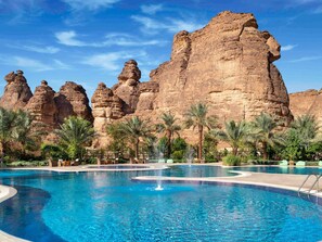A swimming pool with a fountain, palm trees, and rock formations in the background. - Shaden Resort (Al-'Ula)