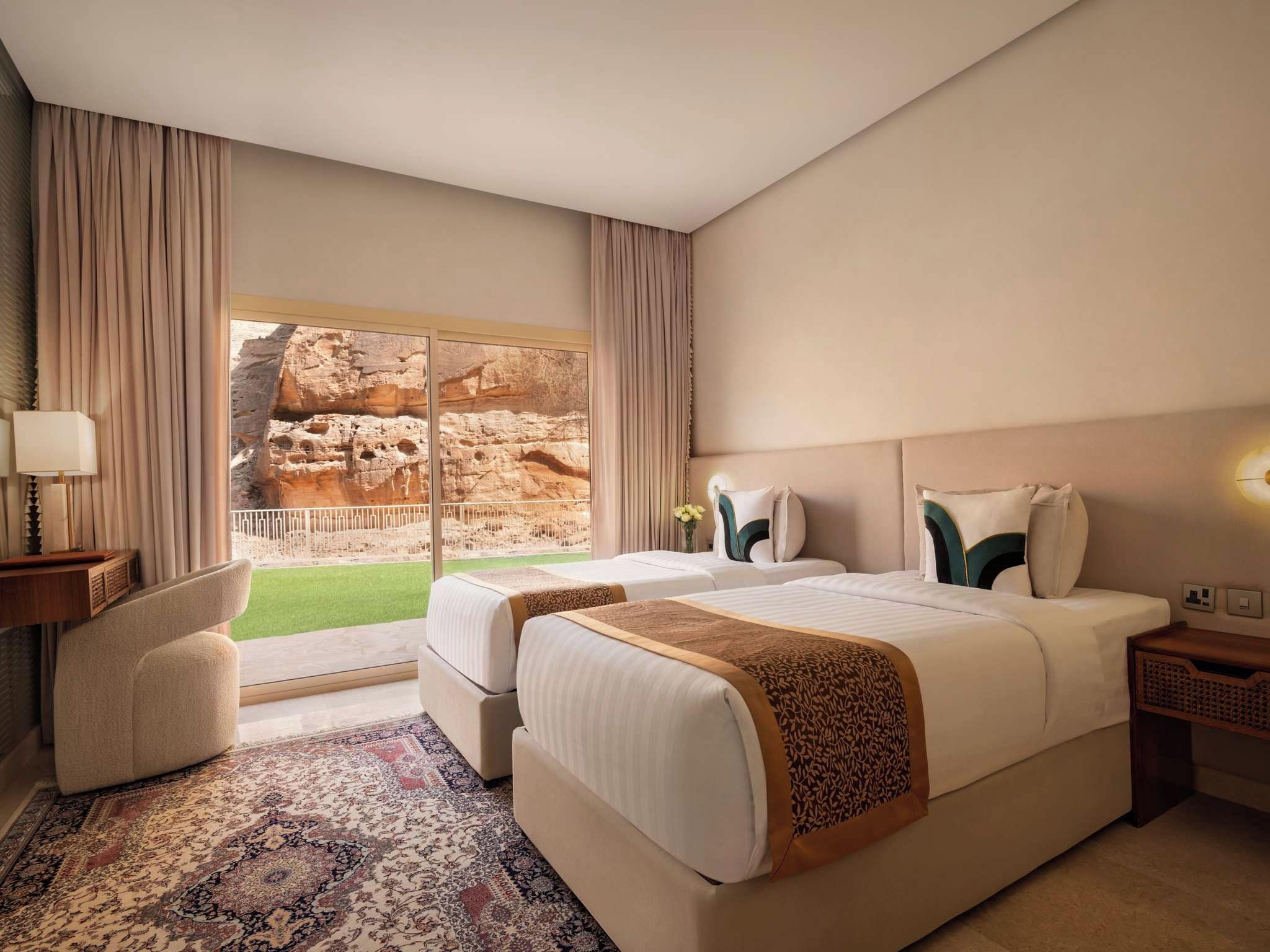 Habitación de hotel con dos camas, zona de estar, un ventanal con vistas a formaciones rocosas y una alfombra estampada.