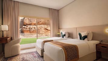 Habitación de hotel con dos camas, zona de estar, un ventanal con vistas a formaciones rocosas y una alfombra estampada.