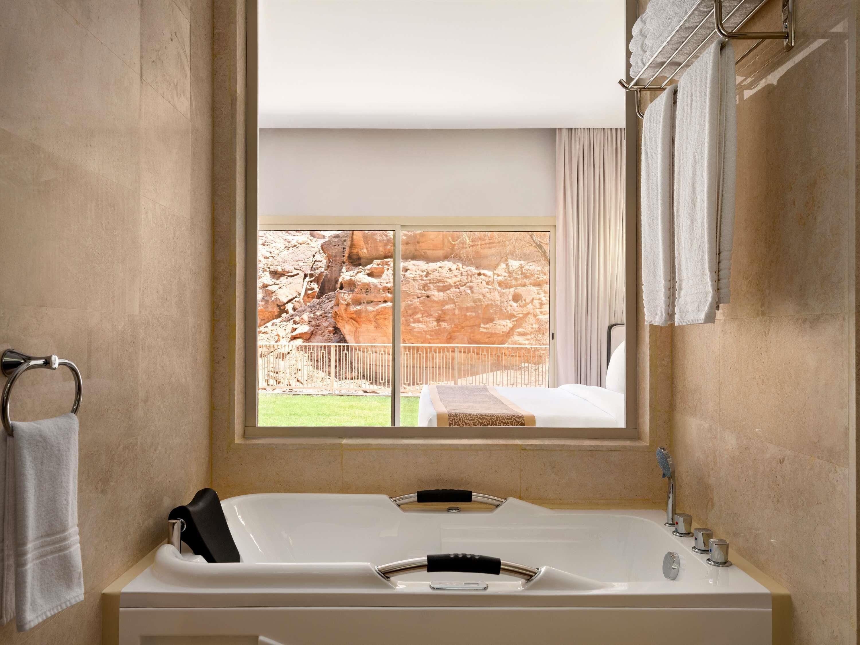 Un baño con una bañera grande, una ventana con vistas a terreno rocoso y un perchero para toallas.