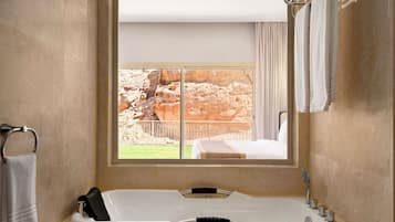 Un baño con una bañera grande, una ventana con vistas a terreno rocoso y un perchero para toallas.