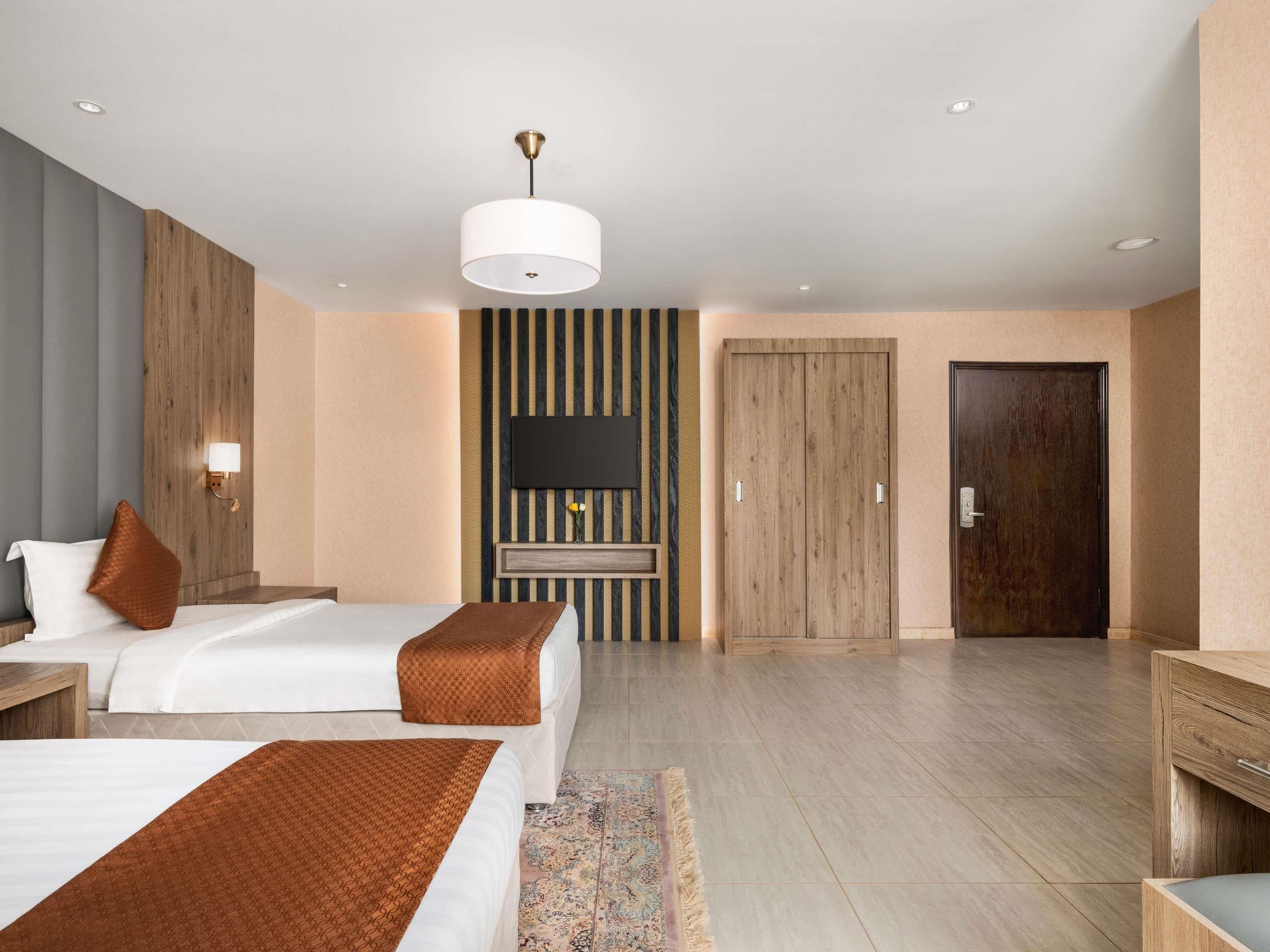 A hotel room with two beds, a flat-screen TV, a wooden wardrobe, and a small desk.