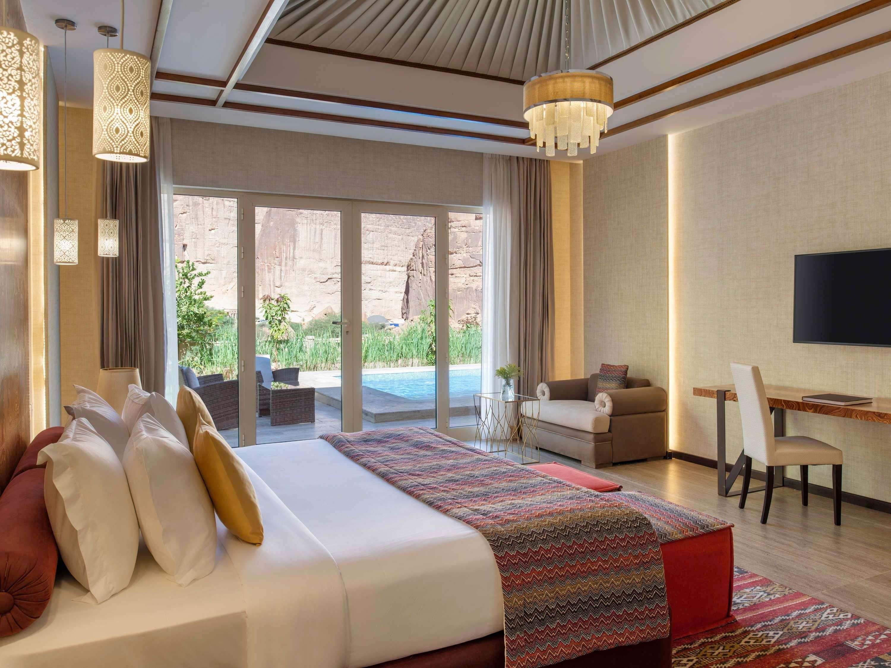 Ein Hotelzimmer mit Bett, Schreibtisch, Fernseher und Blick auf Pool und Außenbereich.