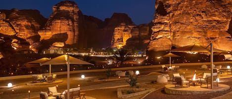 Un resort en el desierto de noche, con zonas de estar al aire libre, piscina y formaciones rocosas iluminadas.