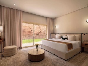 Una habitaci ón de hotel con una cama grande, una mesita redonda de madera, una mesita de noche y vistas a un área exterior cercada.