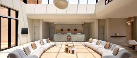 A spacious lounge area with a central seating arrangement, a reception desk, and a large skylight.