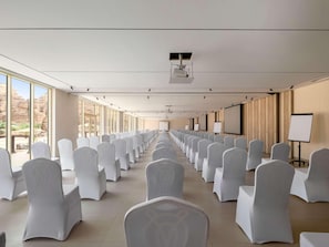 Una sala conferenze con file di sedie bianche, ampie finestre e un proiettore a soffitto.