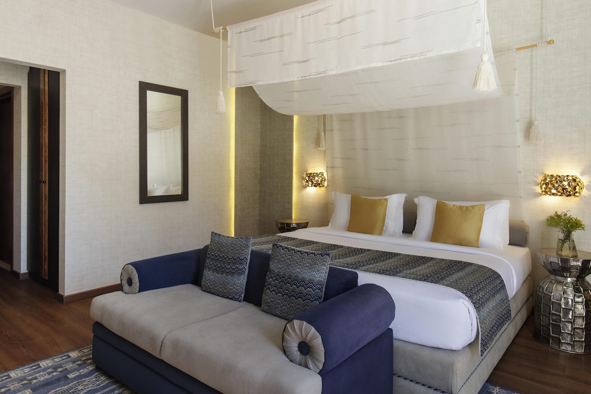 Una habitación de hotel moderna con una cama, un sofá, un espejo y luces decorativas en la pared.