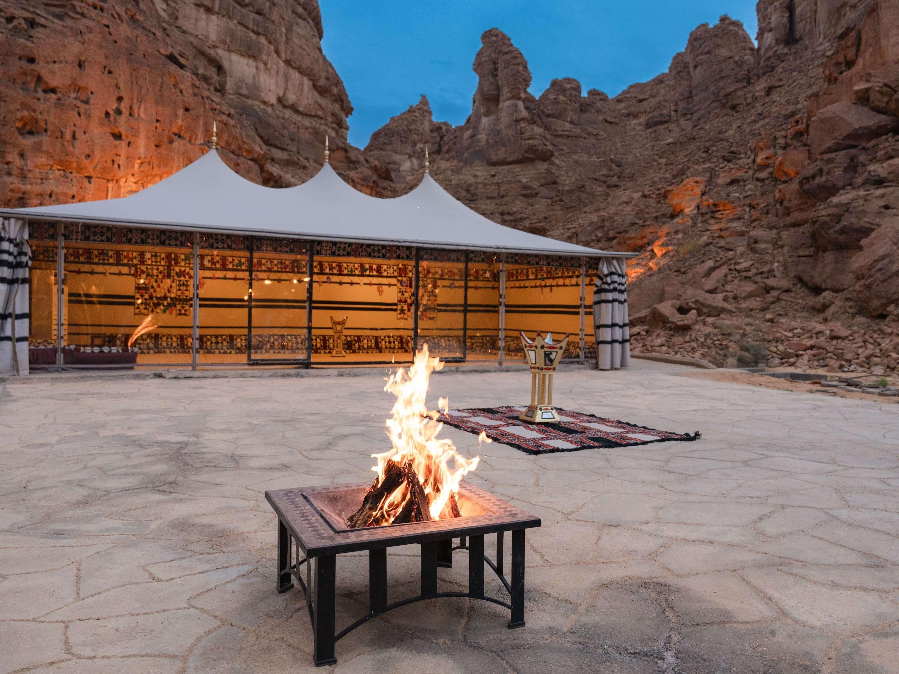 A fire pit in an outdoor area with a tent in the background.