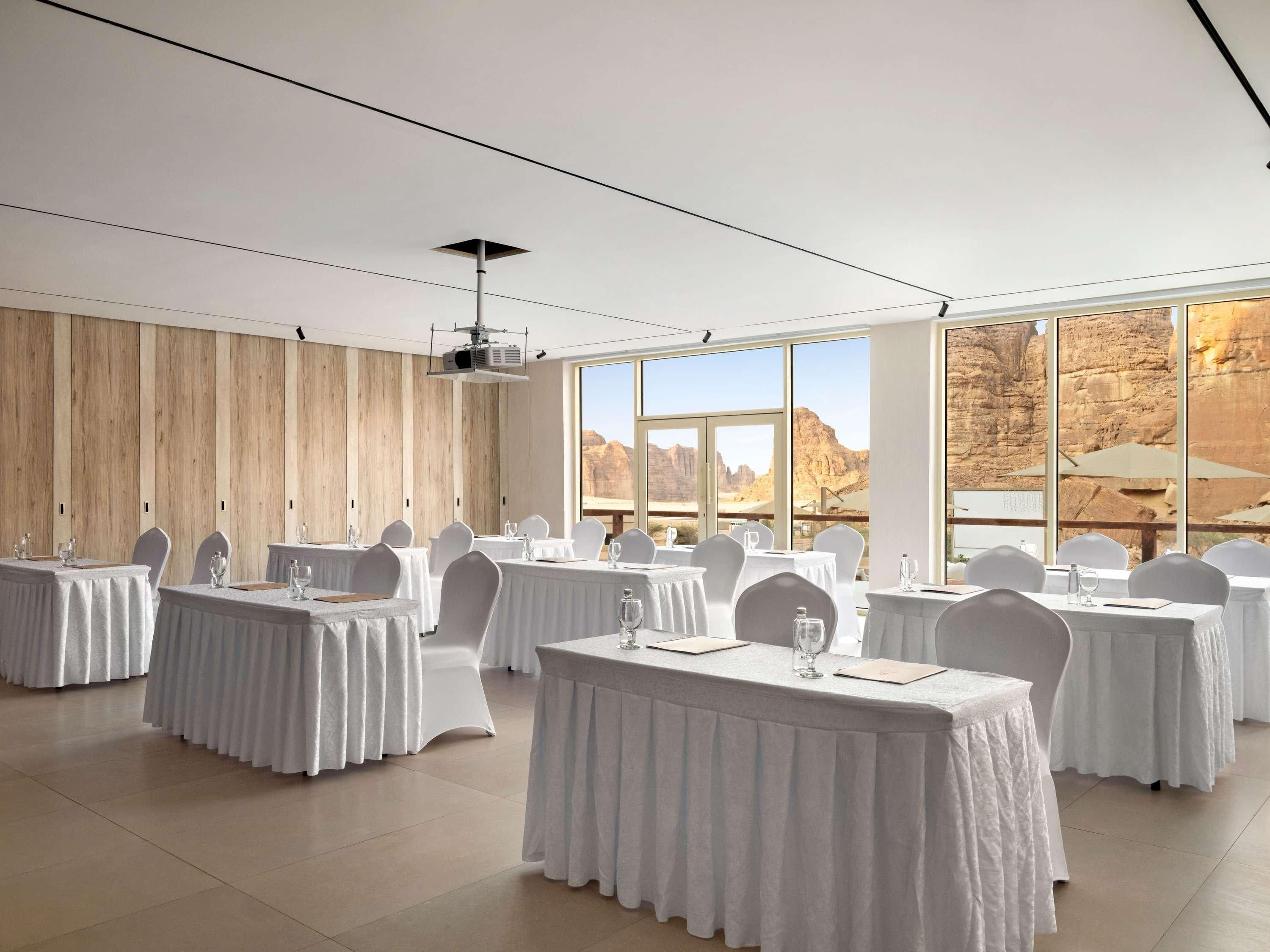 Une salle de conférence avec des tables disposées pour une réunion, de grandes fenêtres donnant sur le désert et un projecteur fixé au plafond.