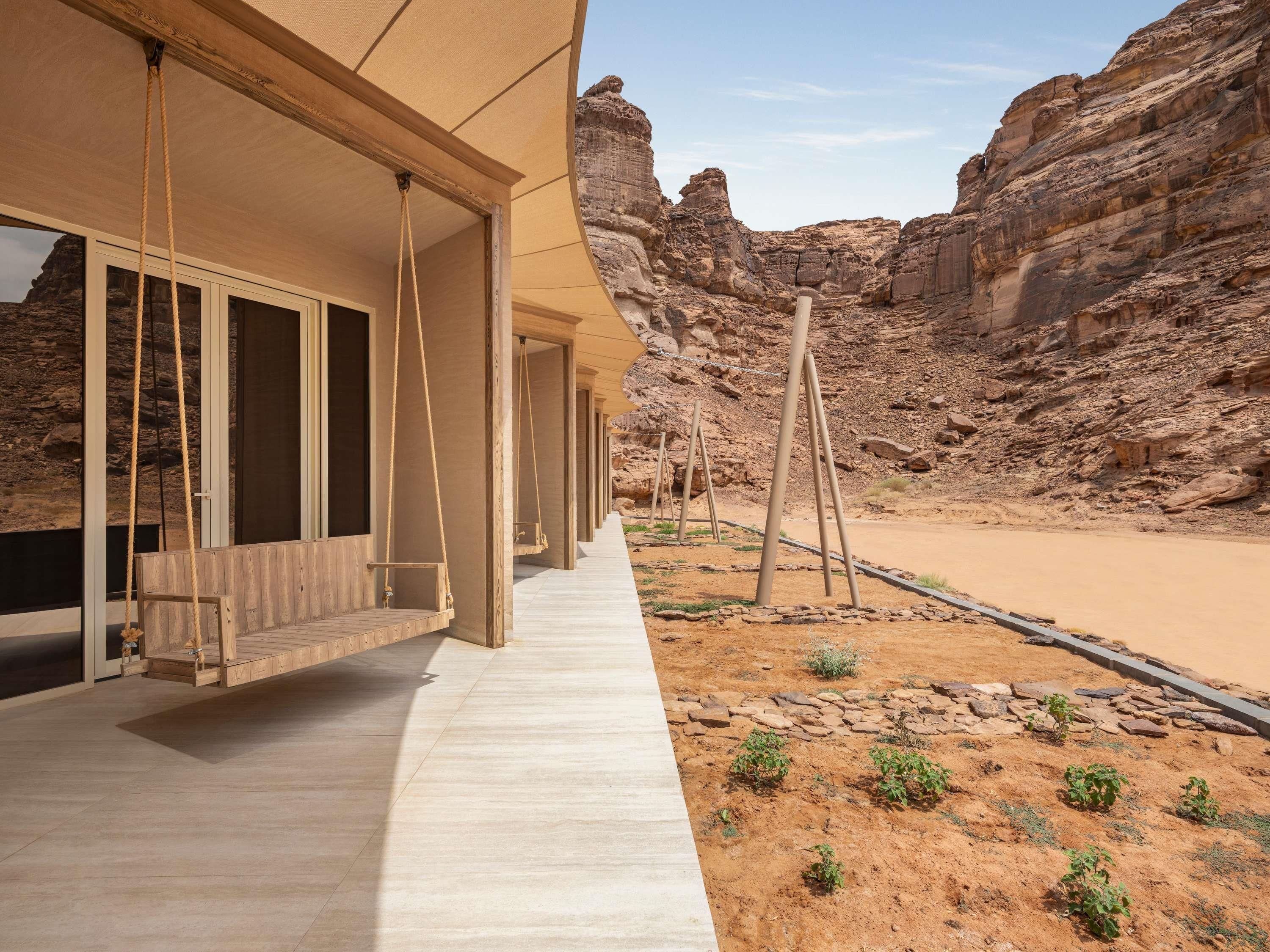 Ein Wüstenresort mit Holzterrasse, großen Fenstern und Blick auf steilen Fels.