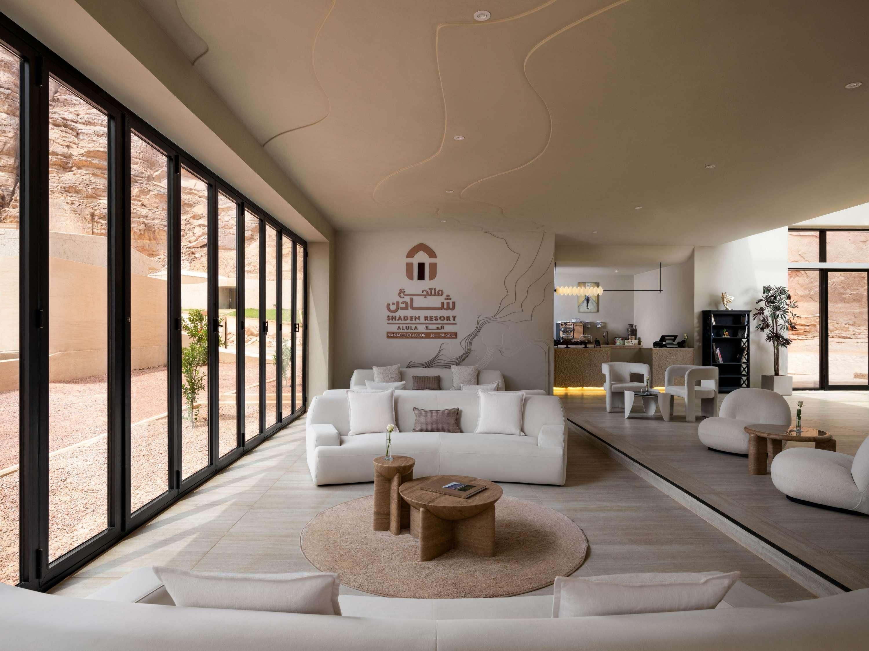 A modern living room with a large window, a reception desk, and a kitchen in the background.