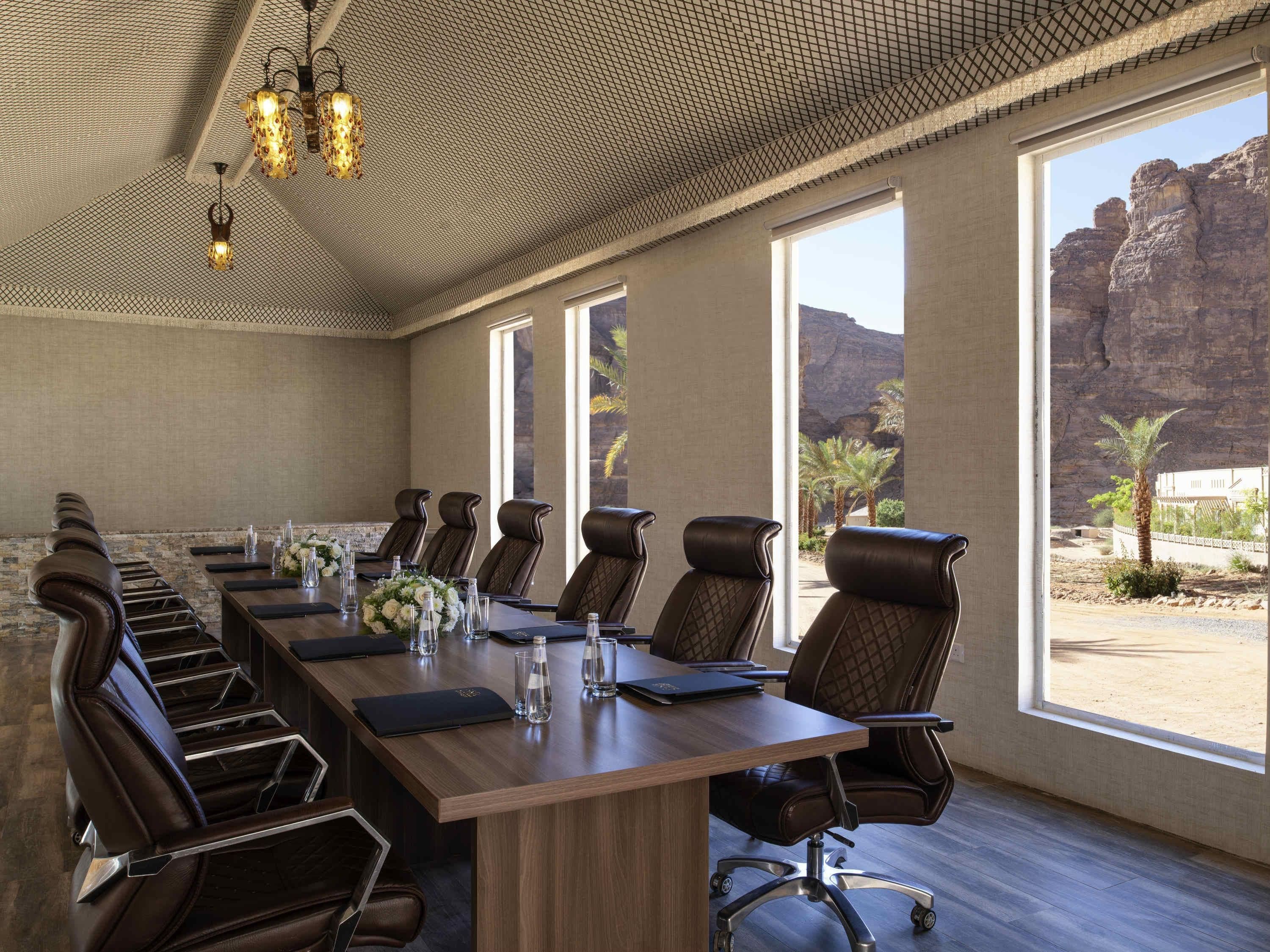 Un salón de conferencias con una larga mesa, sillas de cuero y ventanas amplias con vista a terreno rocoso.