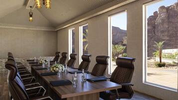 Un salón de conferencias con una larga mesa, sillas de cuero y ventanas amplias con vista a terreno rocoso.