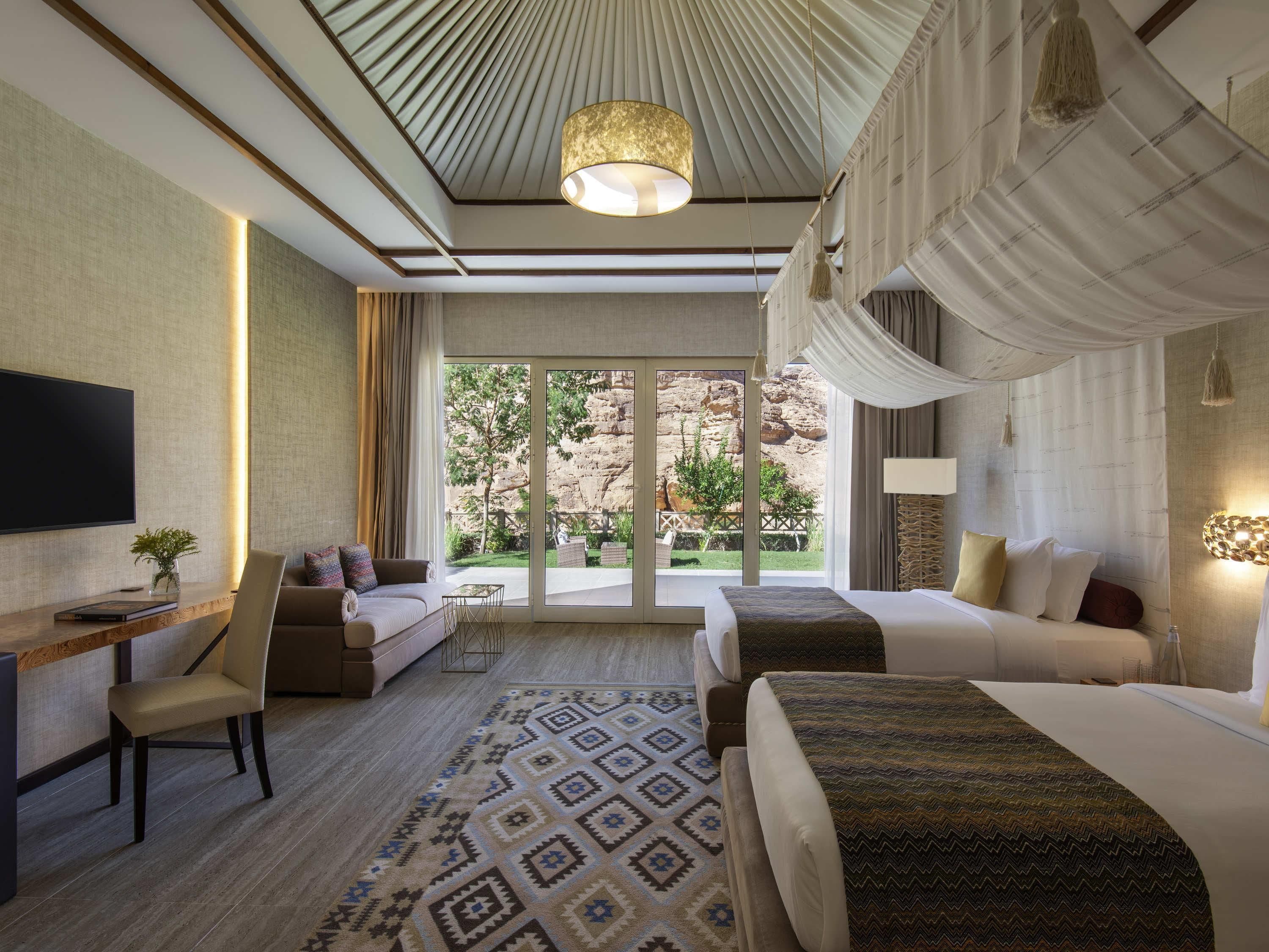 A hotel room with a large bed, a desk, a chair, a TV, and a view of the outdoors.