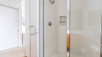 A modern bathroom with a glass shower enclosure, a white sink, and a small shelf with toiletries.