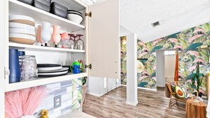 Cozinha com armários brancos, bancada de mármore e área de jantar com papel de parede tropical.