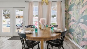 Uma sala de jantar com mesa redonda de madeira, cadeiras pretas e um papel de parede tropical.