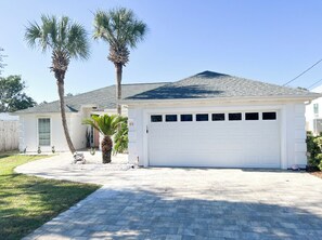 A single-story house with a white garage door, a paved driveway, and two palm trees. - Steps to the beach & Close to 30A! Private pool & putting golf ☀️🏖️⛳️ 18+ to book (Panama City Beach)