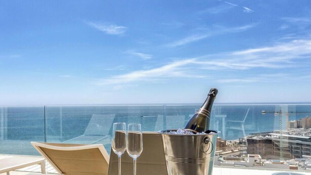 A balcony with a clear view of the ocean, a champagne bottle in a bucket, and two champagne glasses. - Nova | Panoramic Sea View - Pool (Fuengirola)