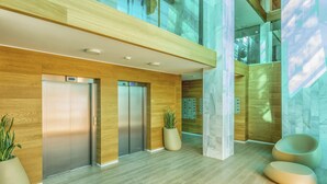 A modern lobby with a wooden floor, two elevators, a large potted plant, and a hanging sculpture. - Nova | Panoramic Sea View - Pool (Fuengirola)