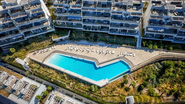 En vy från ovan av ett modernt hotell med en central pool, flera balkonger och en frodig trädgårdsanläggning.