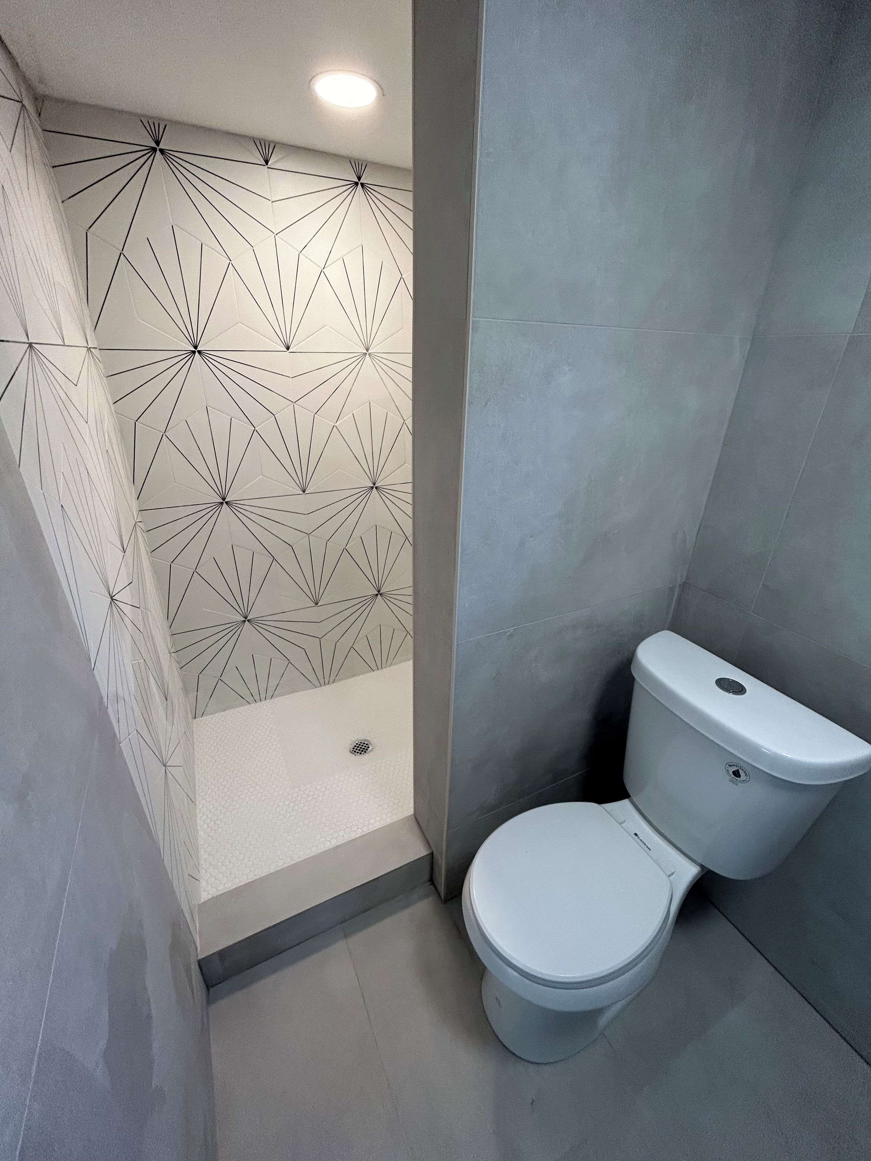 A modern bathroom with a geometric patterned shower wall, a toilet, and a tiled floor.