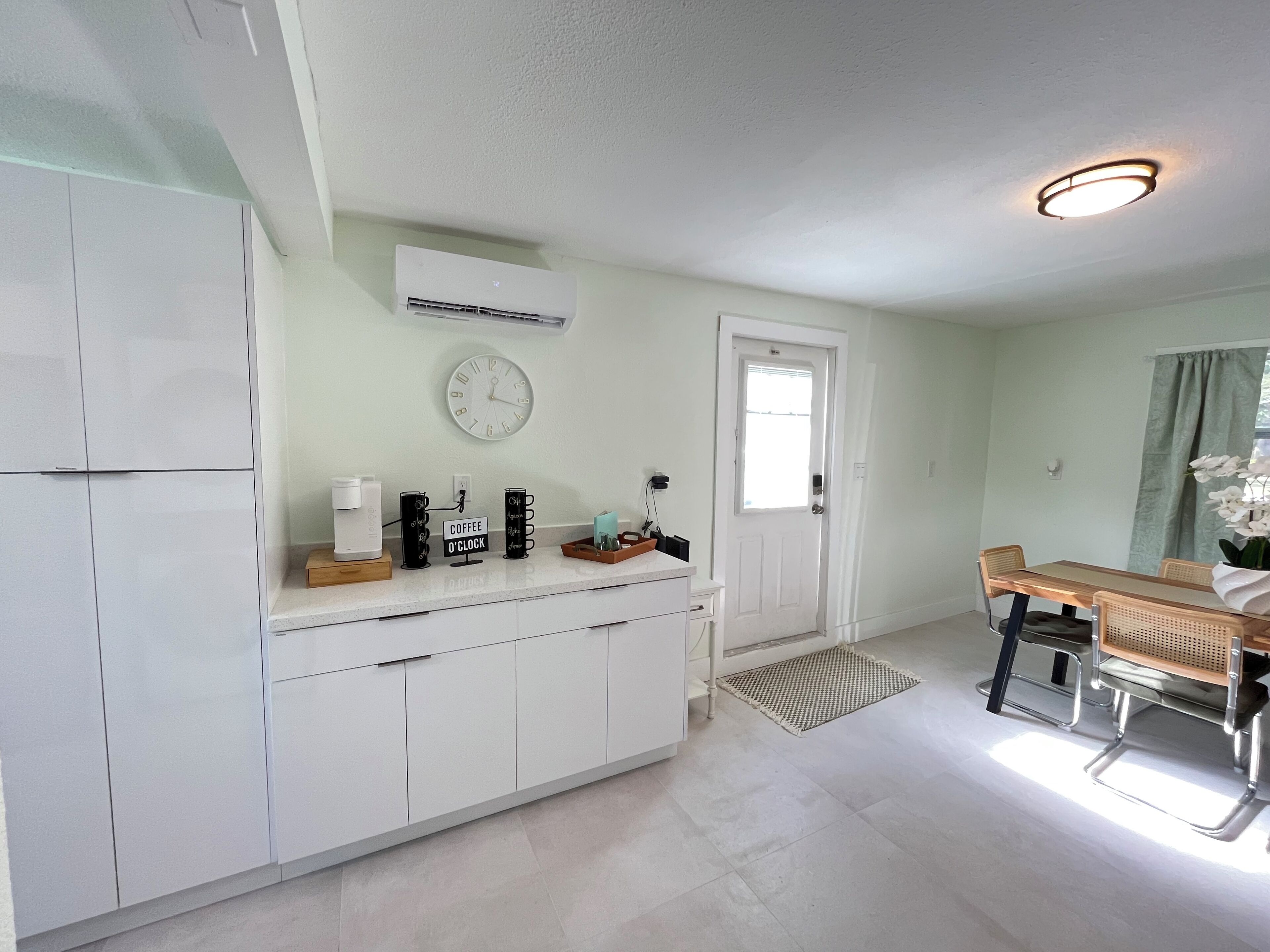A modern kitchen with white cabinets, a coffee station, and a dining area with a wooden table and chairs.