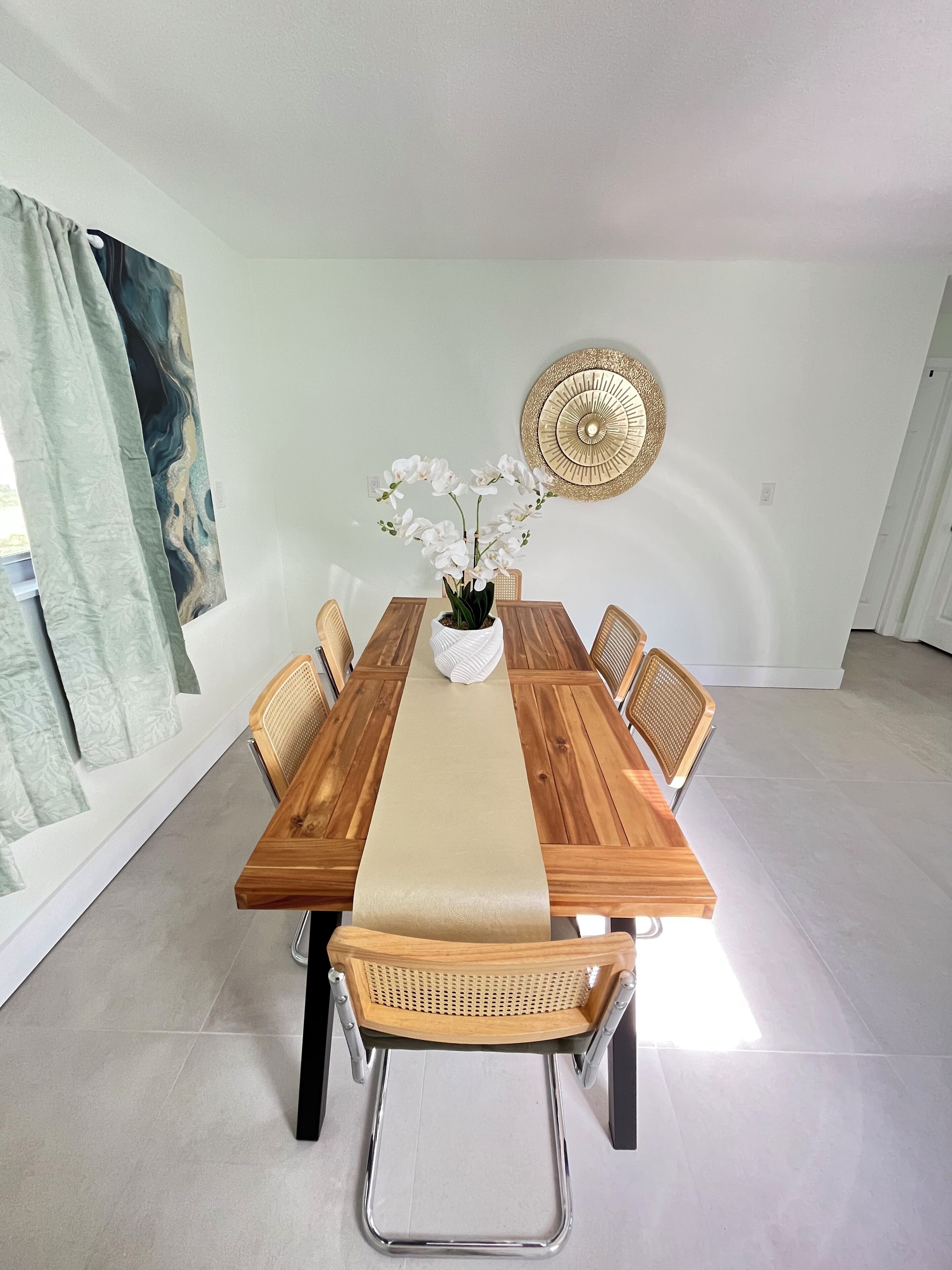 A dining area with a wooden table, white chairs, a vase with white flowers, and a decorative wall piece.