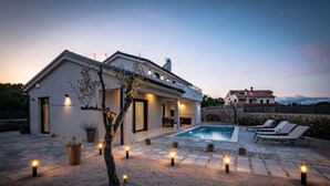 A modern house with a swimming pool, outdoor lighting, and a stone wall.