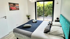 A modern bedroom with a large bed, a view of greenery through a sliding door, and a painting on the wall. - Villa Canopée 6P - Piscine Chauffée/fibre/clim (Gujan-Mestras)
