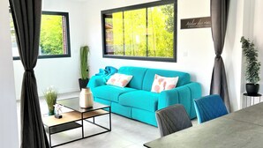 A modern living room with a teal sofa, a coffee table, and a dining table. - Villa Canopée 6P - Piscine Chauffée/fibre/clim (Gujan-Mestras)