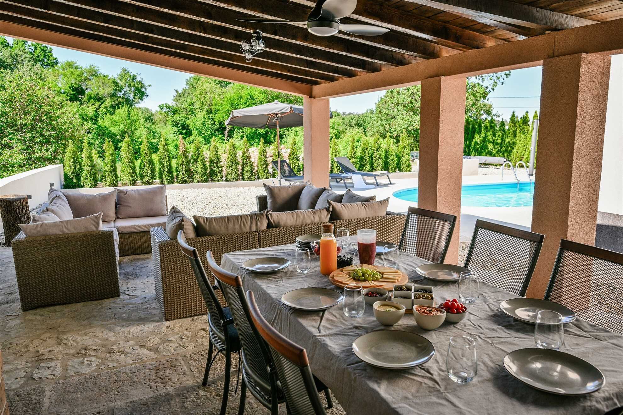 Ein Essbereich im Freien mit Blick auf einen Pool, einer überdachten Terrasse und Korbmöbeln.