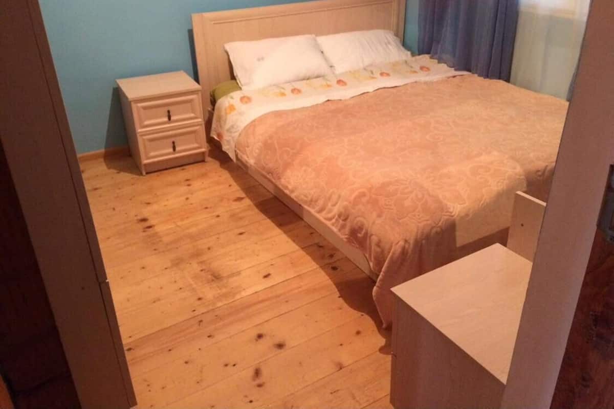 A bedroom with a wooden floor, a bed with a patterned bedspread, a nightstand, and a dresser.