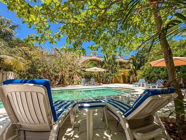 A pool area with lounge chairs and umbrellas, surrounded by tropical vegetation.